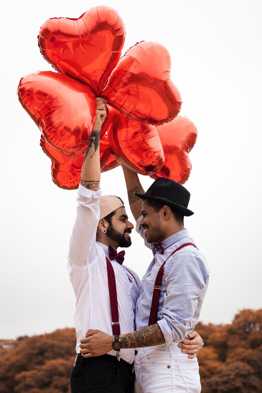 two men holding red heart balloons